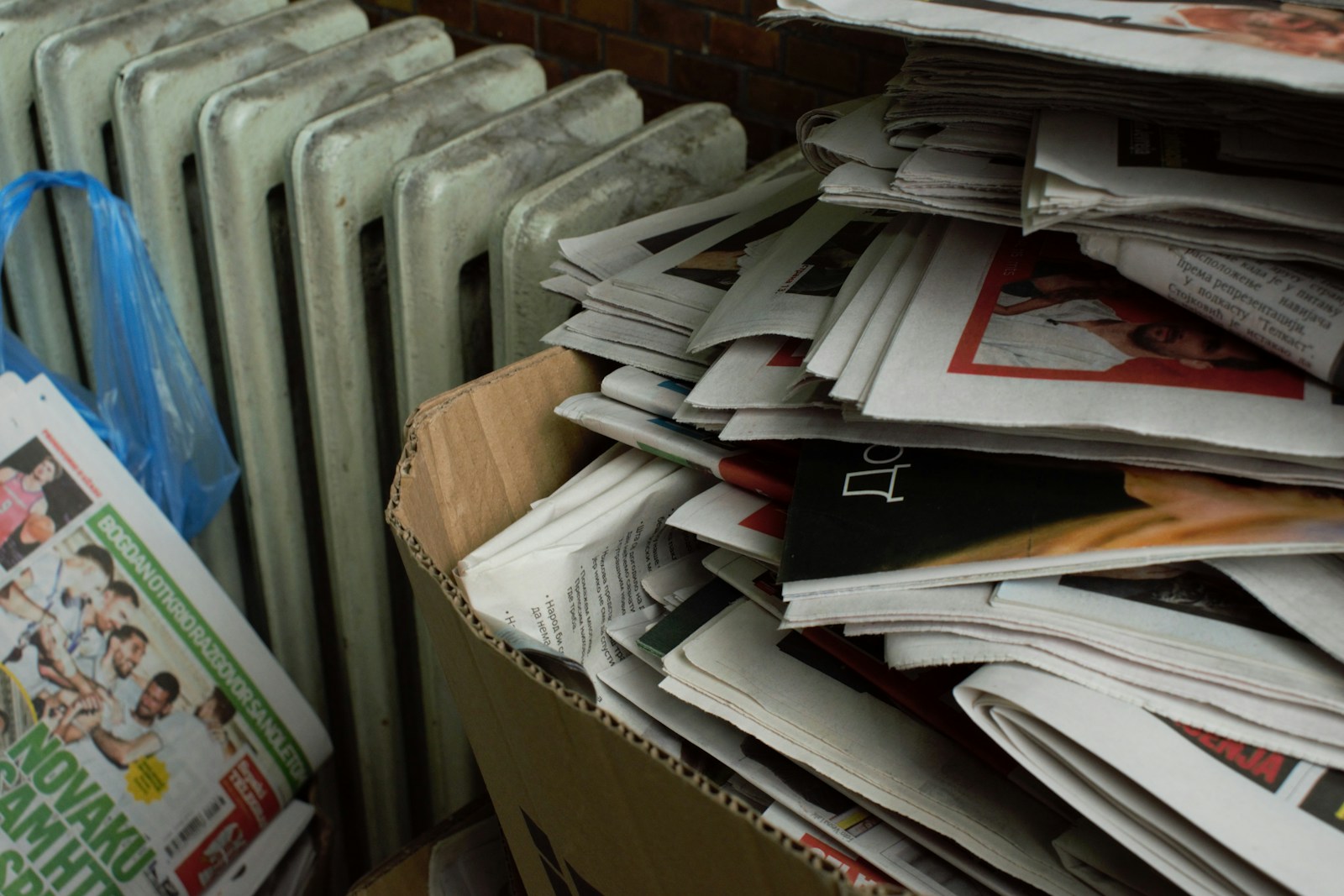 a cardboard box full of newspapers next to a radiator